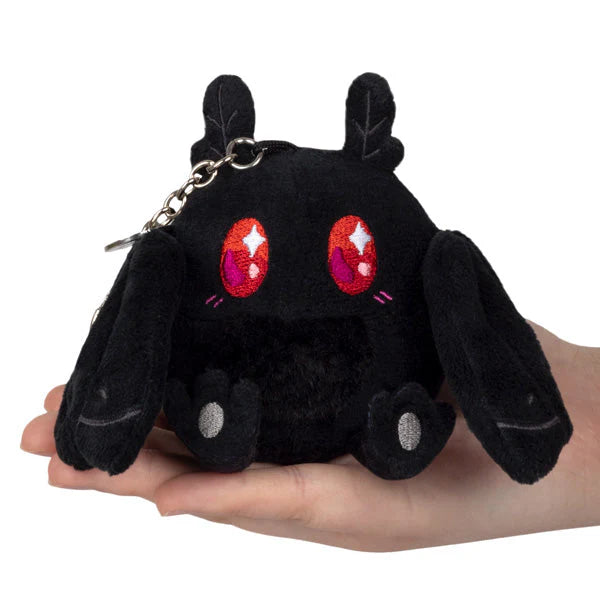 Micro Squishable Baby Mothman plush with large red eyes, floppy ears, and keychain held in a hand.