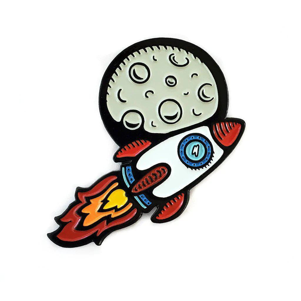 Kolorspun Pins To The Moon Rocketship enamel pin featuring a cartoon rocket and cratered gray moon in soft enamel, black metal.