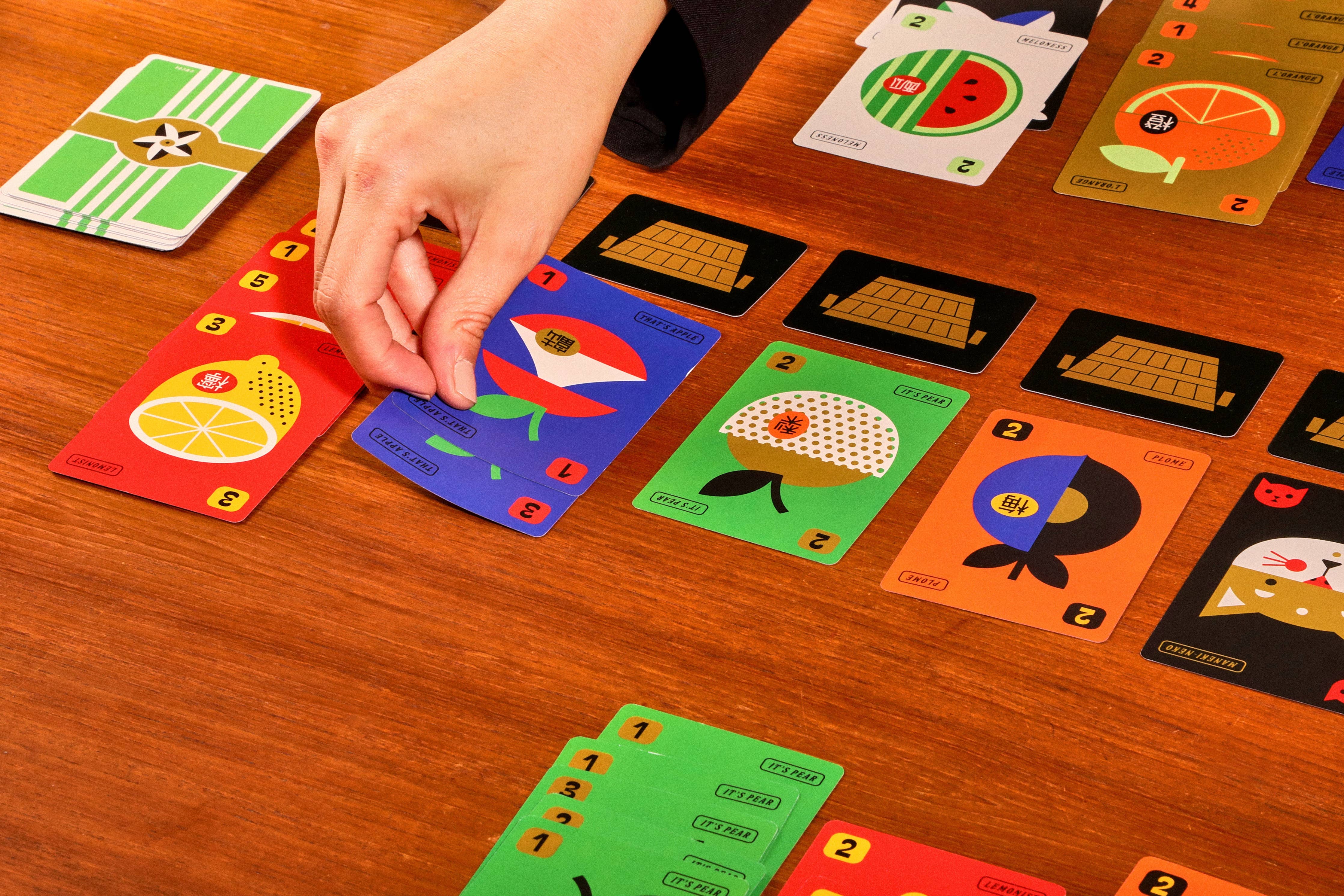 Fruit Boss card game with illustrated fruit cards being played by a hand.