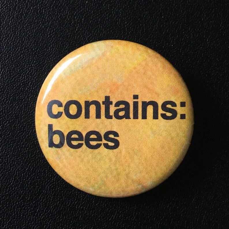 1.25-inch yellow pinback button with Contains Bees and a swarm design on a black textured surface.