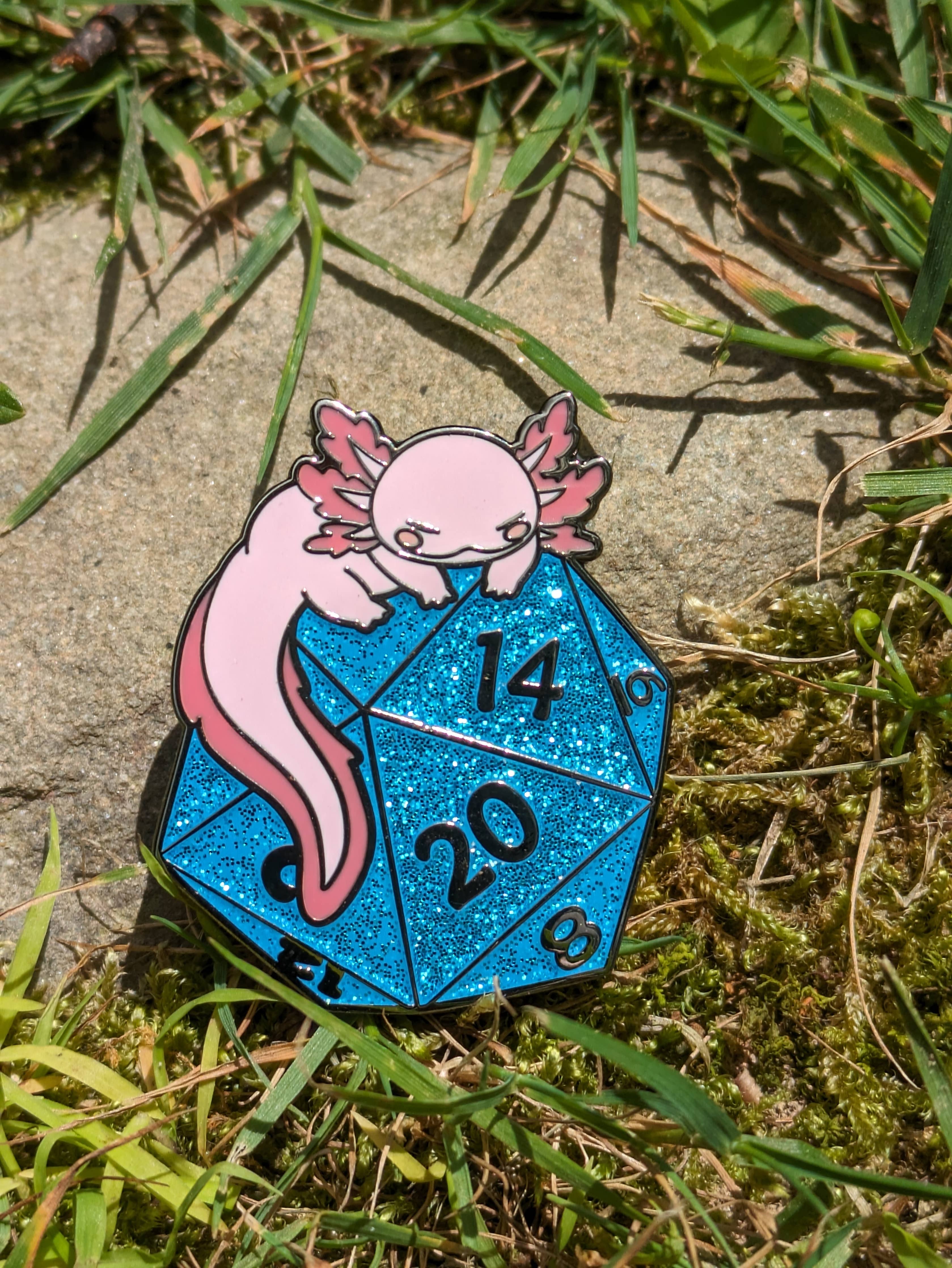 Axolotl on D20 Hard Enamel Pin, 1.5 inches, showing a pink axolotl sitting on a glittery blue 20-sided die.