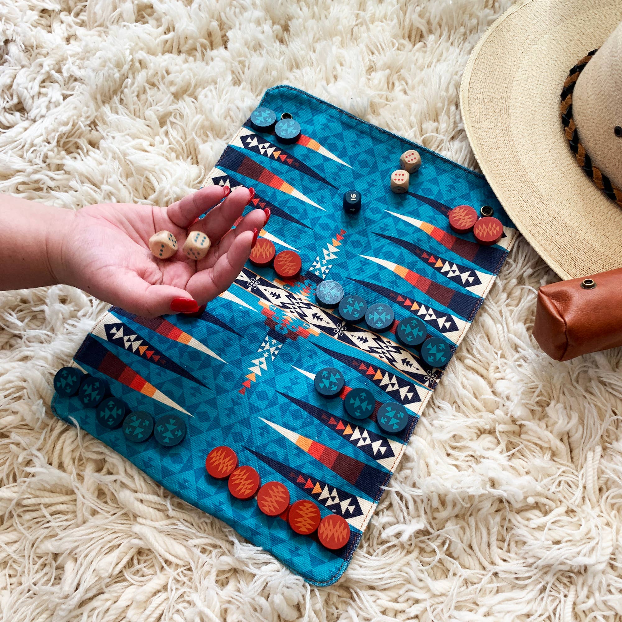 Pendleton Backgammon set with dice in hand, shown on a rug beside a hat and pouch.
