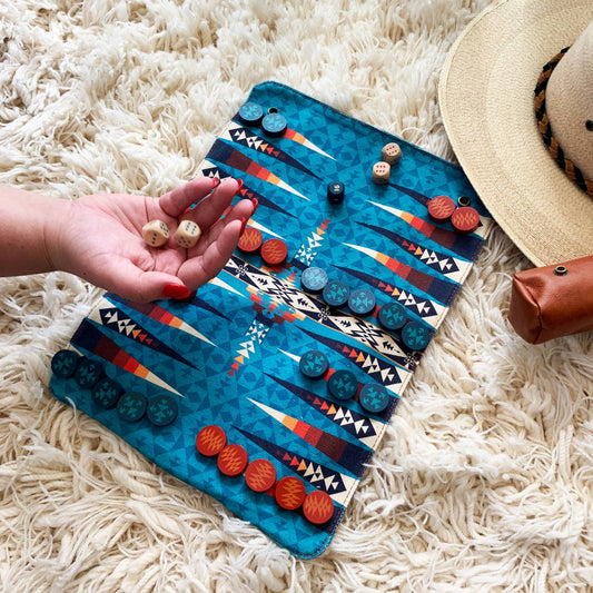 Pendleton Backgammon set with dice in hand, shown on a rug beside a hat and pouch.