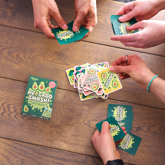 Four people playing Avocado Smash card game at a wooden table, hands holding cards mid-game.