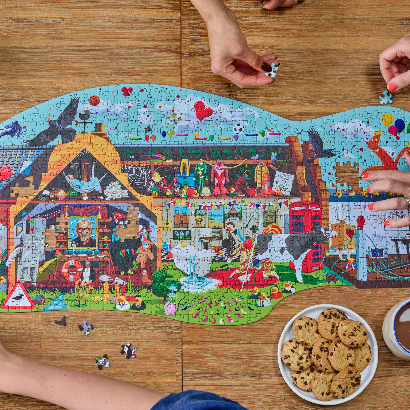 Taskmaster Jigsaw Puzzle (1021 pieces, Secret Task) being assembled on a table; four hands visible; cookies nearby.