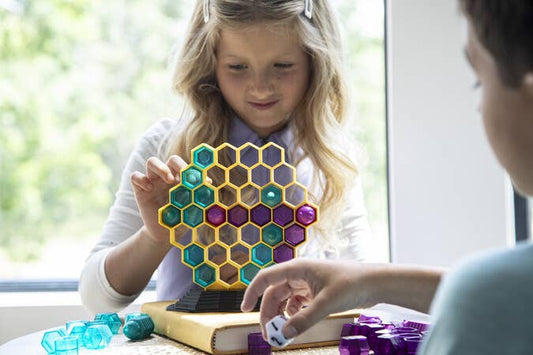Children playing Queen Swarm board game with colorful pieces on a table.