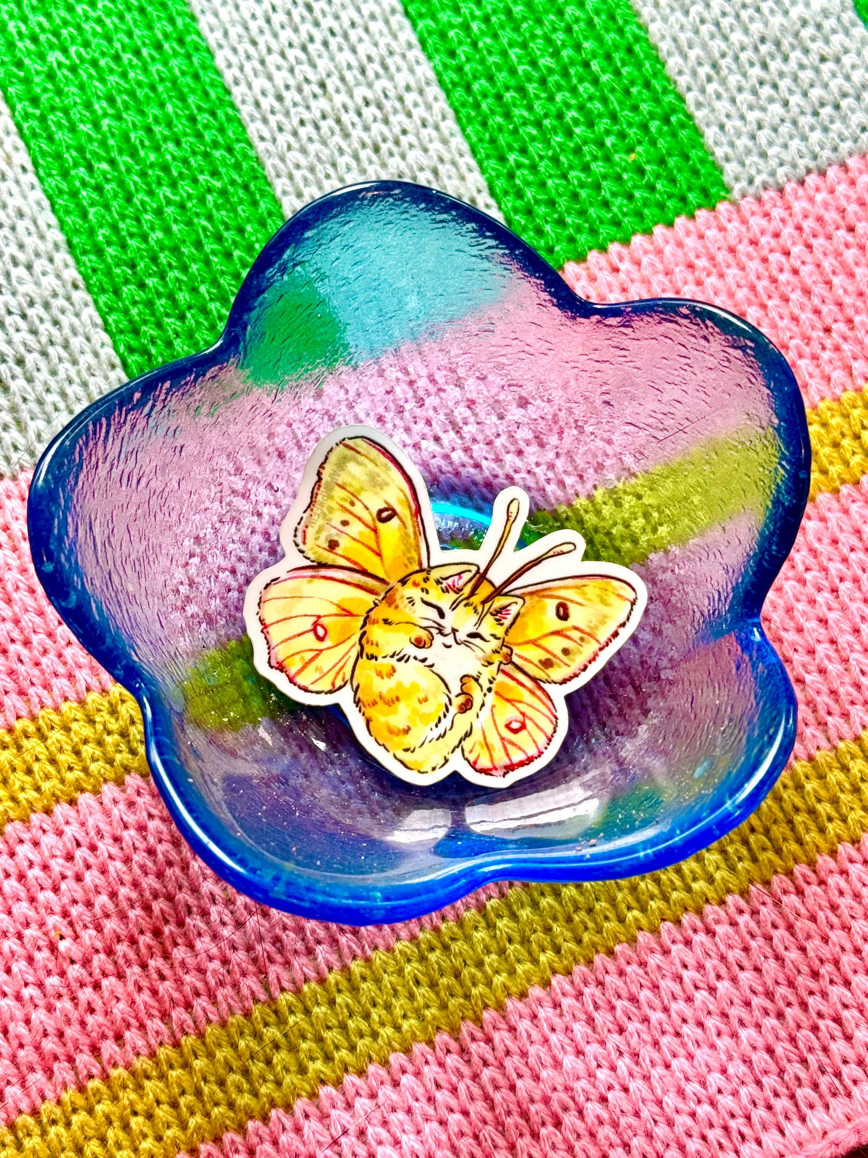 Catterfly sticker: a cat with butterfly wings inside a blue flower-shaped dish.