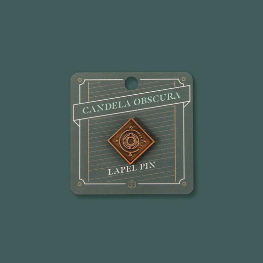 Candela Obscura lapel pin in antique gold with sunburst design and embossed logo.