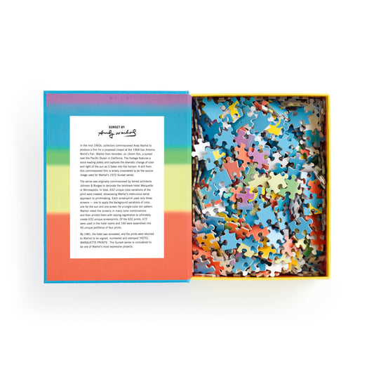 Andy Warhol Sunset 500 Piece Puzzle with open box, colorful pieces, keepsake box, and card with text and signature.