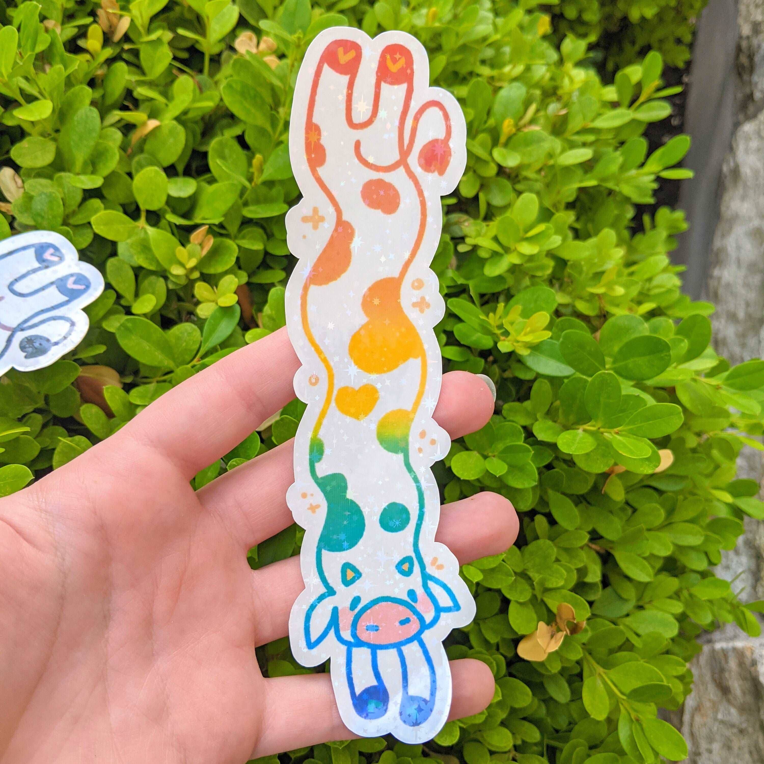 MORE Sparkly Long Cow Sticker with colorful waterproof design held in a hand.