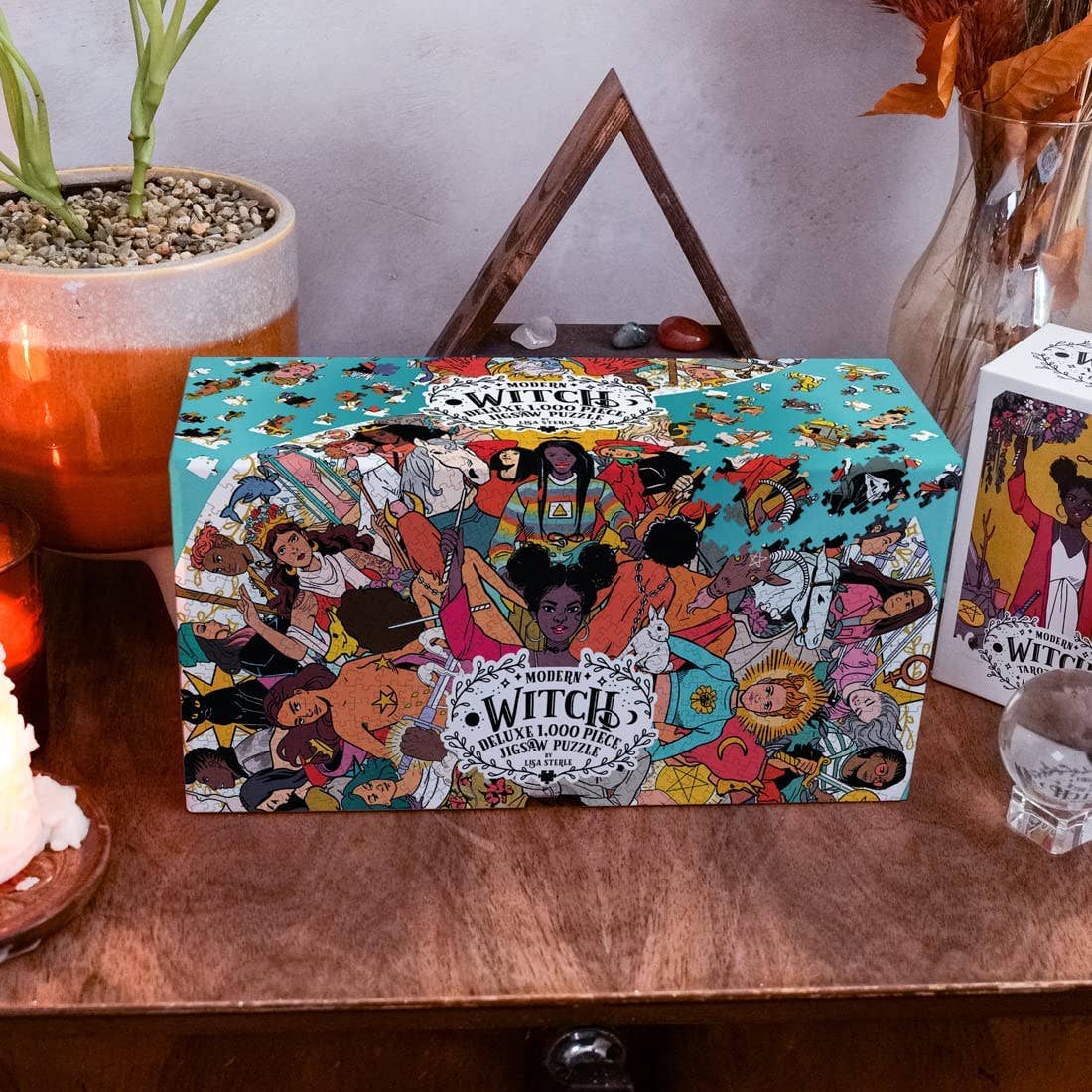 The Modern Witch Deluxe 1,000 Piece Jigsaw Puzzle by Lisa Sterle on a wooden surface with plants.