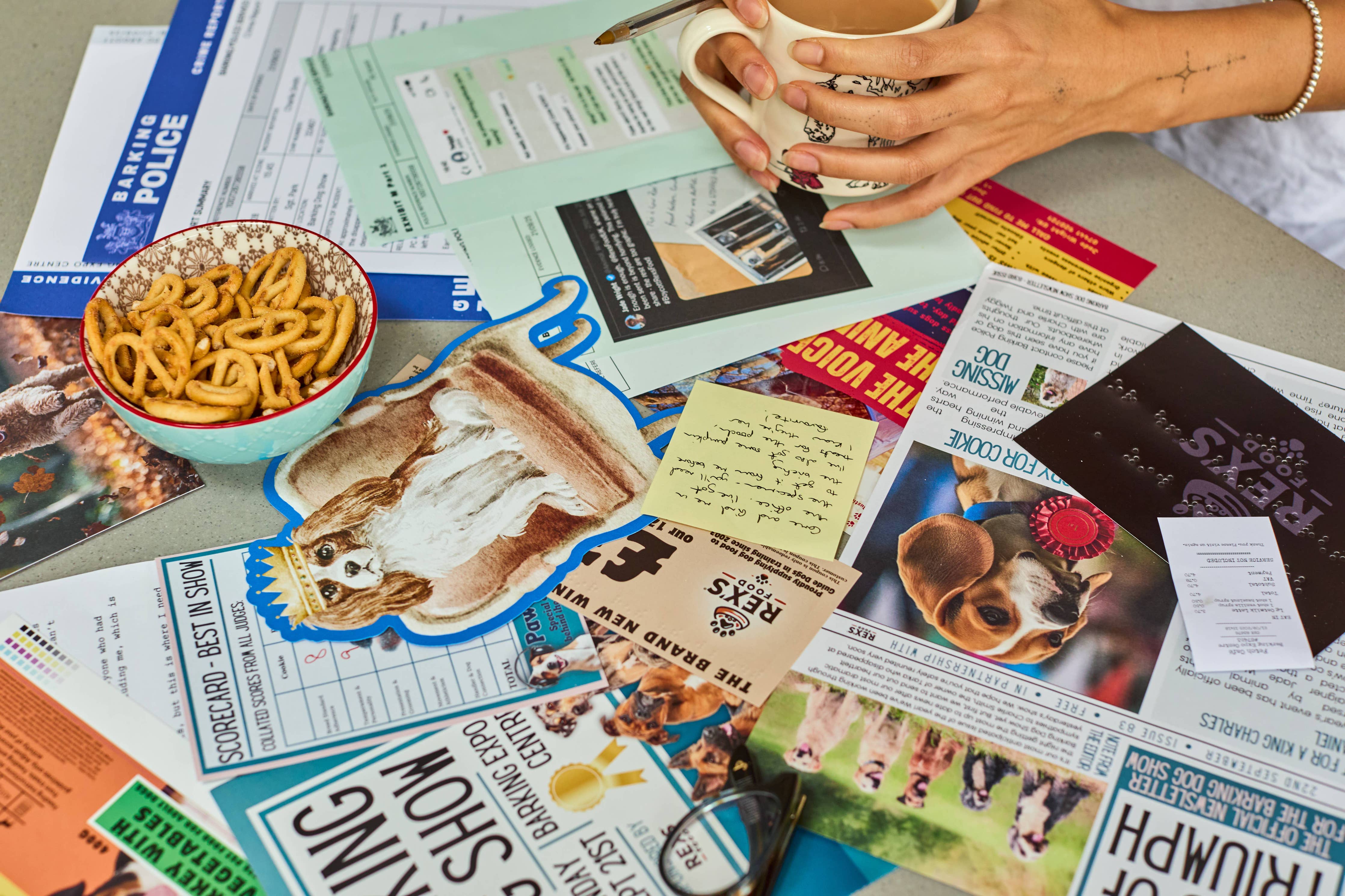 Cold Case: Who Let The Dogs Out? puzzle with papers and pet photos spread on a table; person holds a mug.