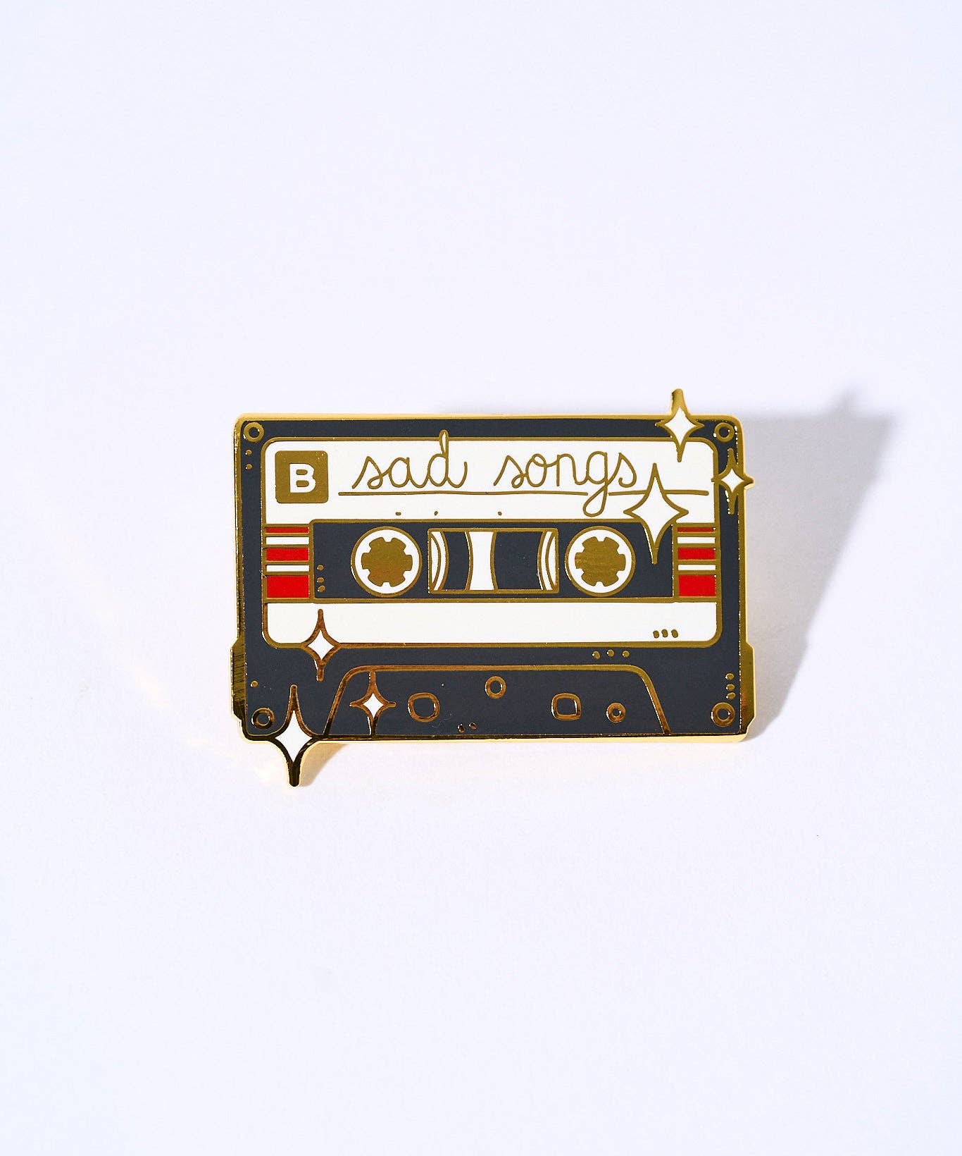Sad Songs pin: a gold-plated enamel cassette tape with sad songs text, a B label, and a clasp backing.
