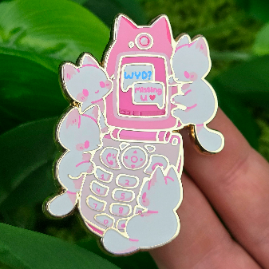 Enamel pin showing four cartoon cats and a flip phone displaying WYD? Missing u, held by a hand.