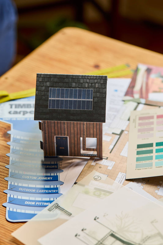 The Affair escape room board game shown with model house and paint swatches on a wooden table.