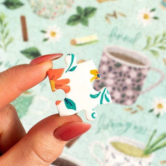 Hand with red nails holds a floral piece from the Tea Time 500 Piece Jigsaw Puzzle.
