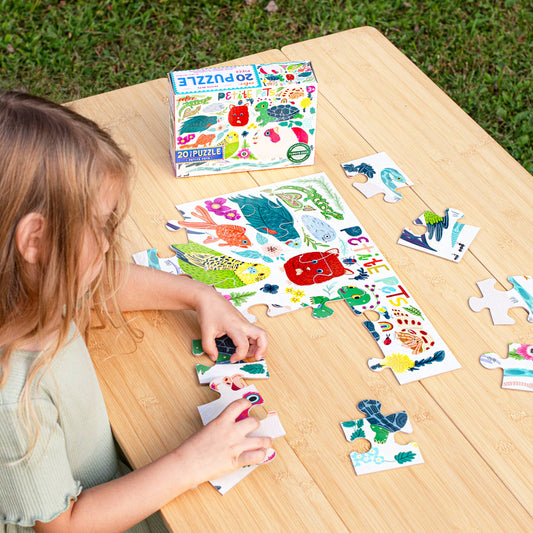 Petite Pets 20 Piece Puzzle being assembled by a child, with the puzzle box nearby on a wooden table outdoors.