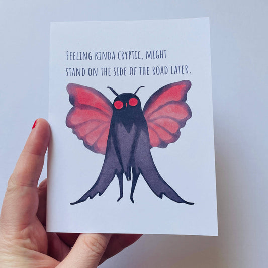 Mothman Cryptic Humor Card displaying a watercolor Mothman and the text Feeling kinda cryptic, held in a hand.