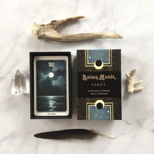 Anima Mundi Tarot Deck, moon card, guidebook, crystal, antler, coral, and feather on white surface.