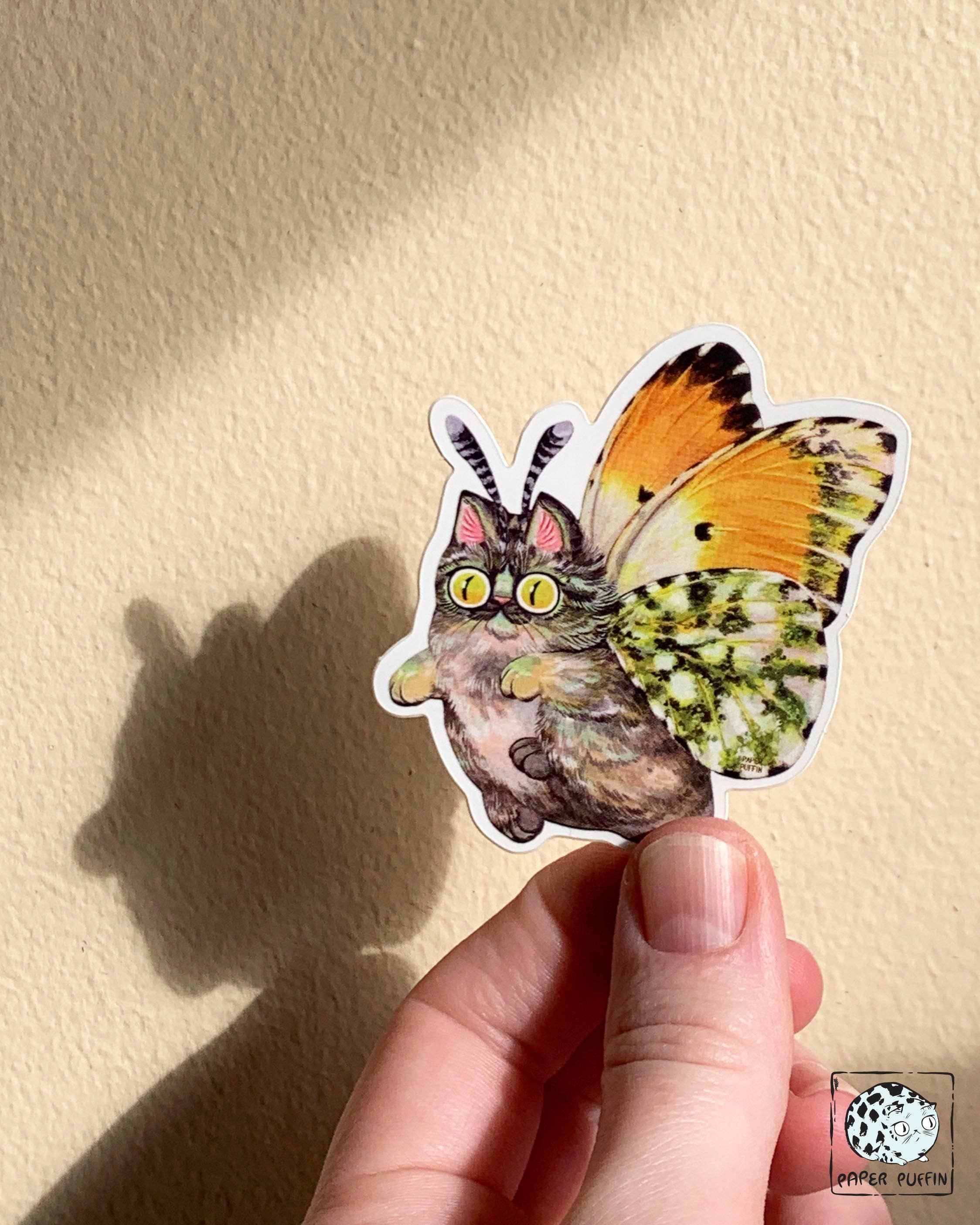 Moth Cat Tippy sticker featuring a fluffy cat with orange-tipped butterfly wings.