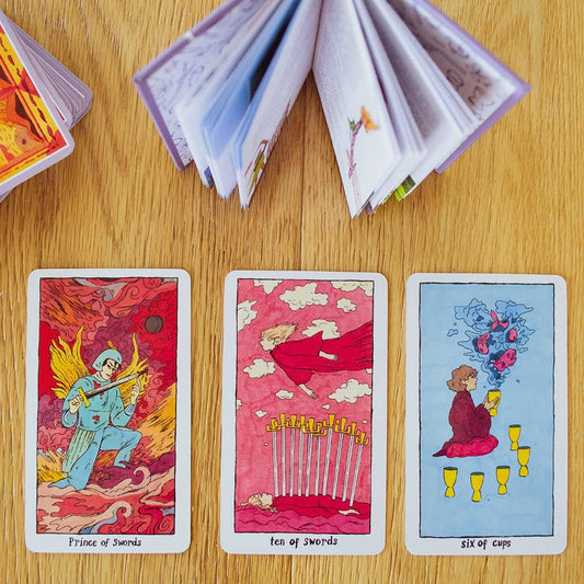 Three Cosmic Slumber Tarot Deck cards displayed on a wooden table with open books above them.