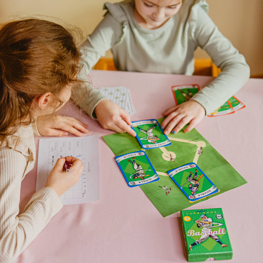 Two children play Baseball Playing Cards at a table; one writes on paper to keep score.