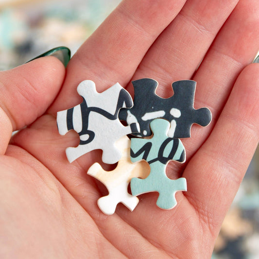Four pieces from the Painted Moons 1,000 Piece Jigsaw Puzzle held in one hand.