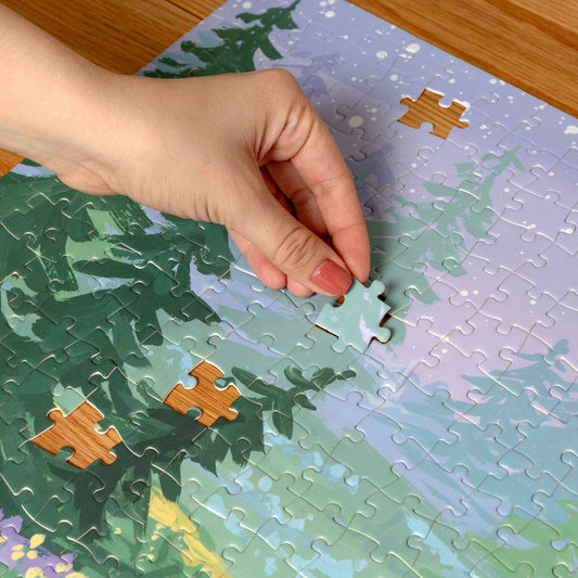 Twilight Garden 500 Piece Jigsaw Puzzle with trees and sky, hand placing a piece.