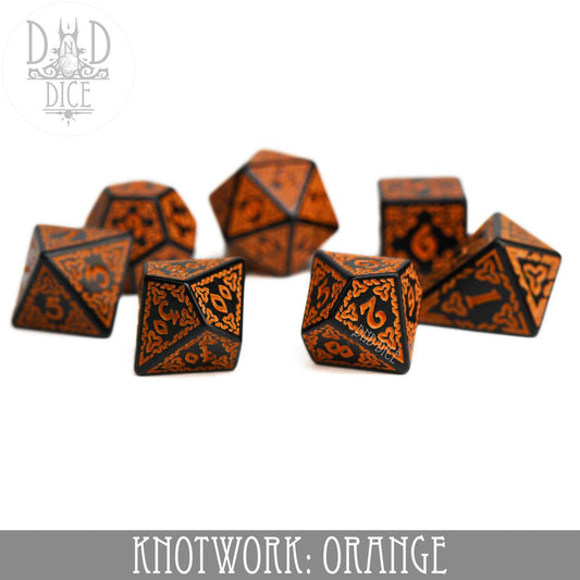 Knotwork: Orange—set of seven black acrylic dice with orange knotwork design, including teardrop D4, on white background.
