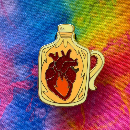 D&D Class Curiosities enamel pin featuring an anatomical heart with flame, displayed on a rainbow tie-dye background.