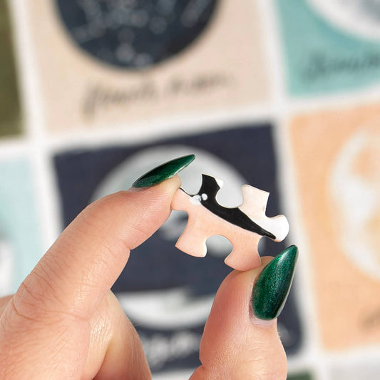 A hand with green nails holds a piece from the Painted Moons - 1,000 Piece Jigsaw Puzzle.