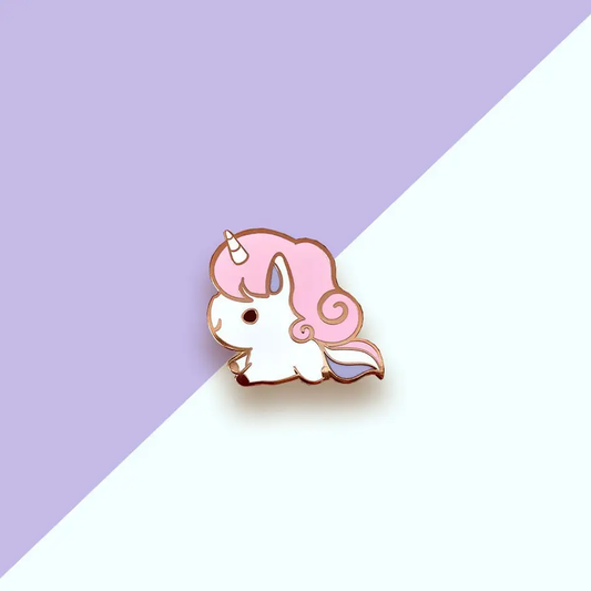 Pink Unicorn Enamel Pin with a pink-maned unicorn on a white base, set against a purple and white diagonal background.