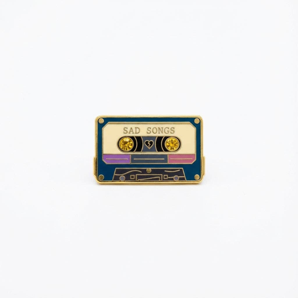 Sad Songs pin (new variant) shaped like a cassette tape with SAD SONGS text, a heart, and two yellow crystals.