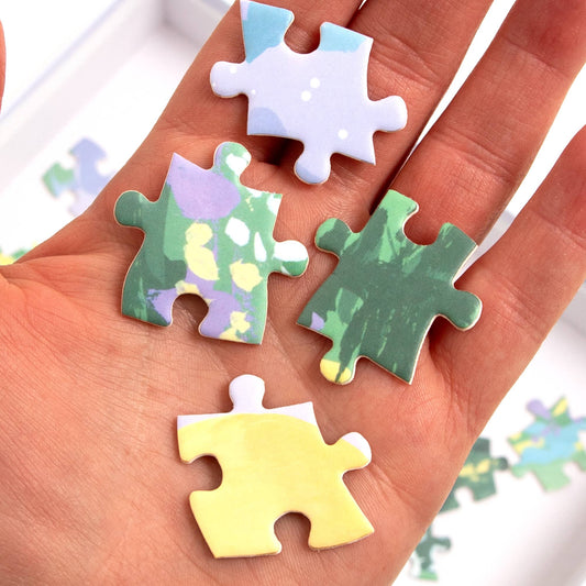 Four colorful pieces from the Twilight Garden - 500 Piece Jigsaw Puzzle displayed on a hand.