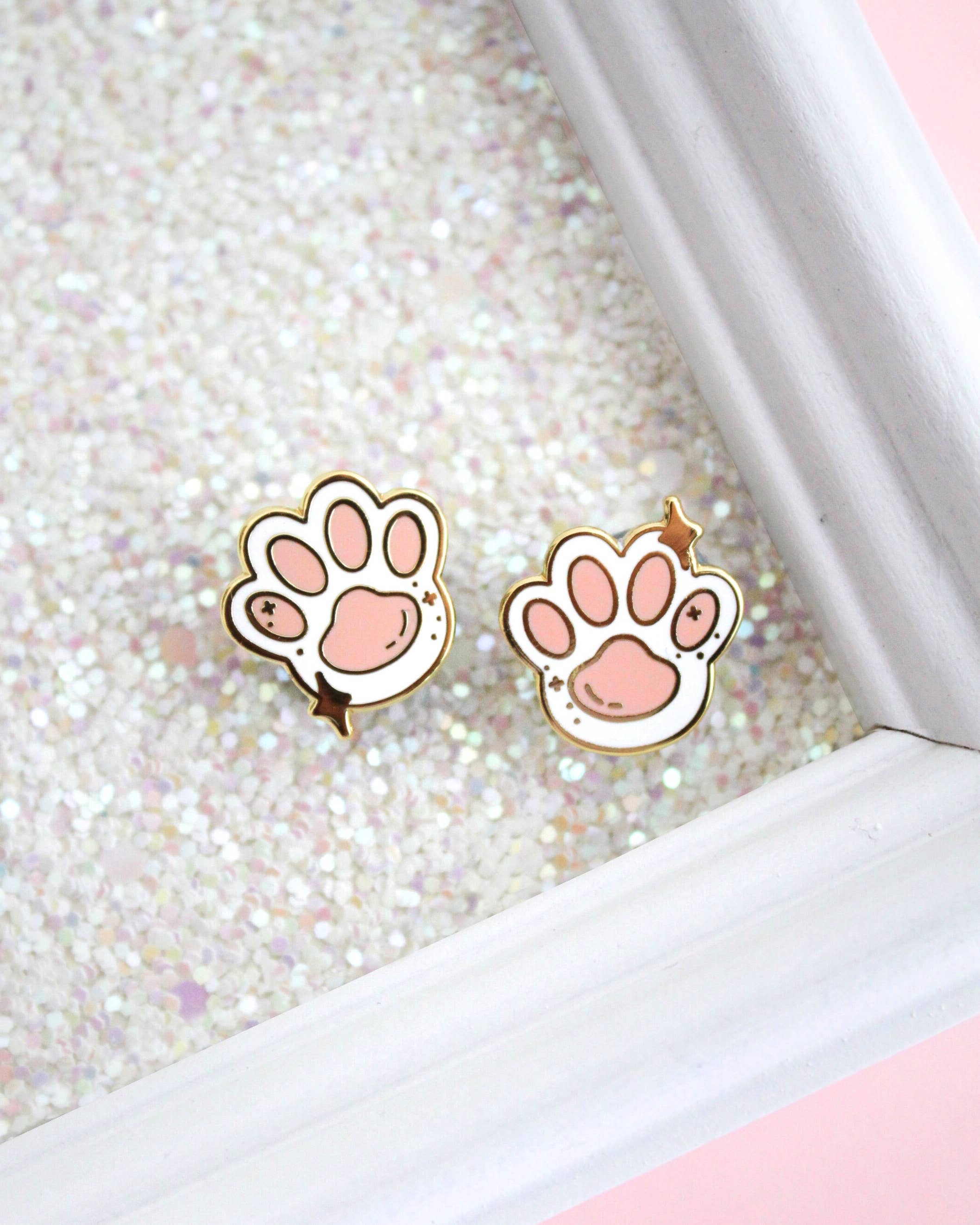 Two Toe Beans enamel pins in pink and white with gold outlines.