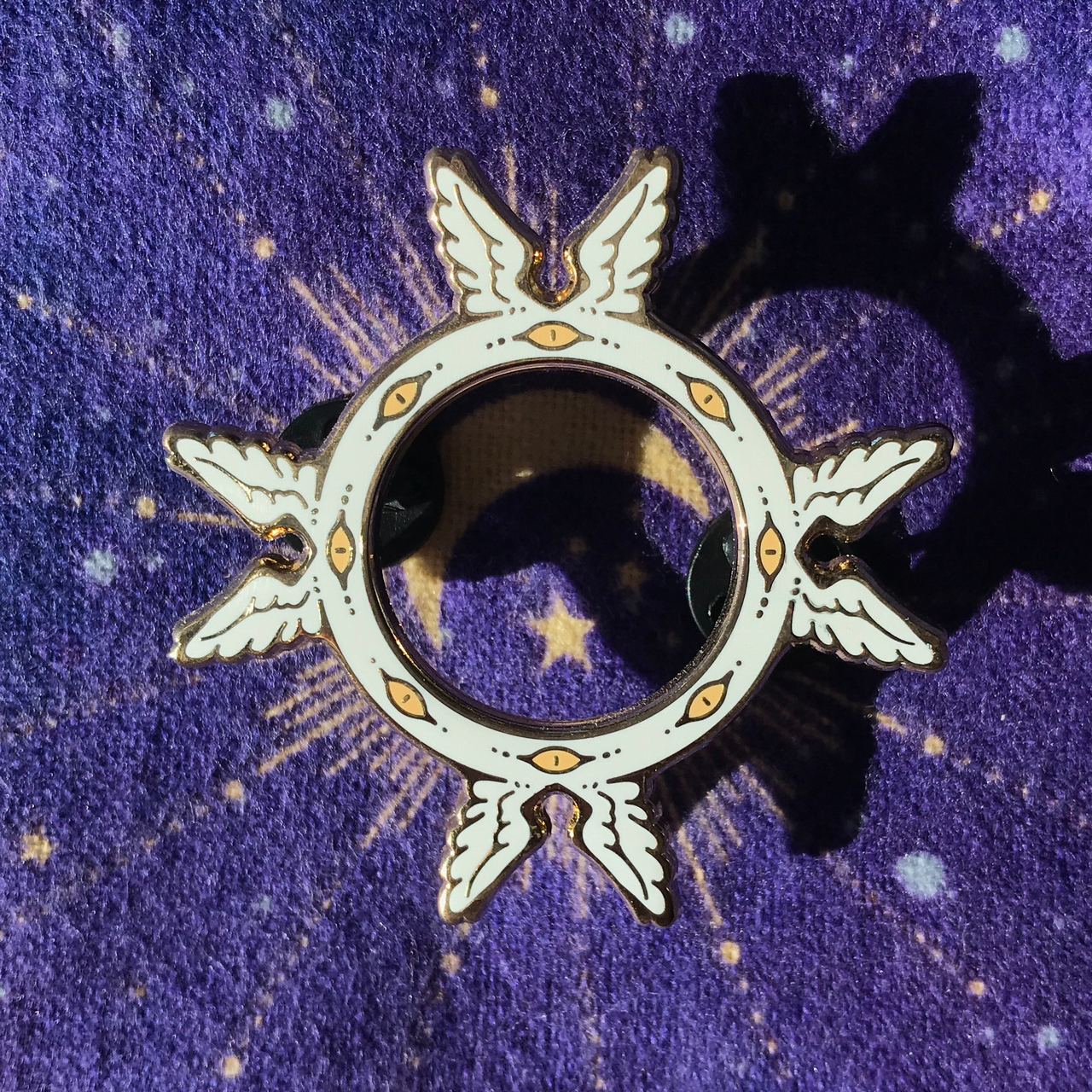 The Eyewheel Pin, a gold plated winged wheel with eyes and four wing pairs.