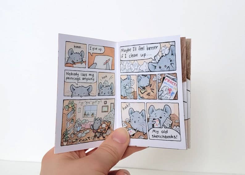The Chinchillustrator Mini-Comic Zine held in hand, showing cartoon mice discussing artists block in a messy room.
