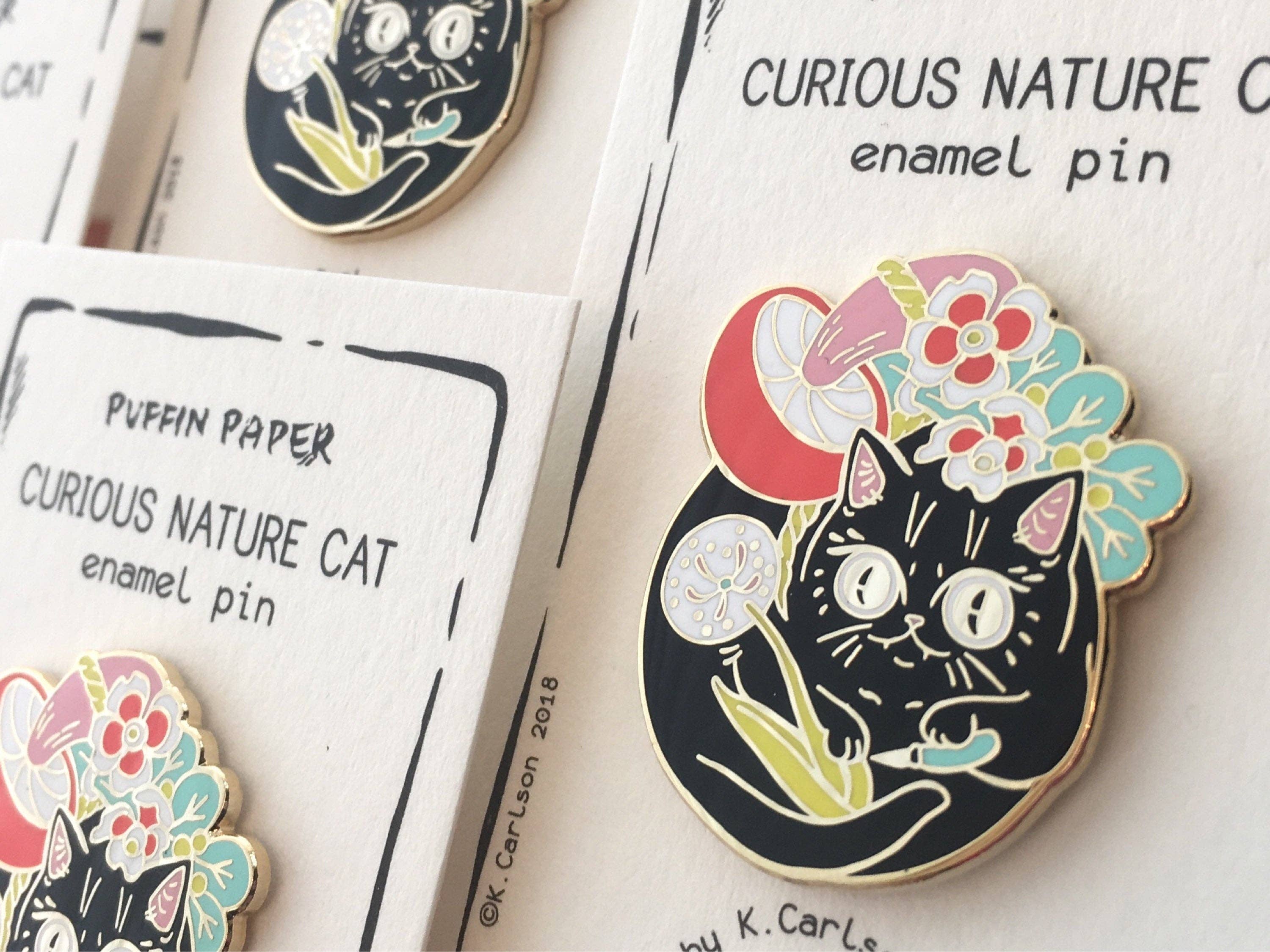 Curious Nature Cat enamel pin: a black cat holding a dandelion surrounded by red, pink, and blue flowers.