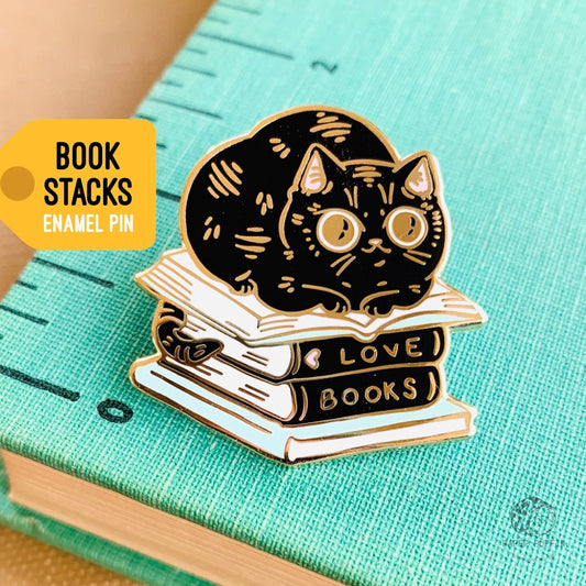 Black cat enamel pin resting on books labeled LOVE and BOOKS.