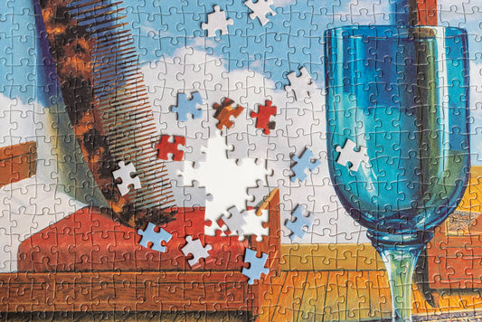 René Magritte Personal Values puzzle with images of a comb, books, blue glass, and some missing center pieces.