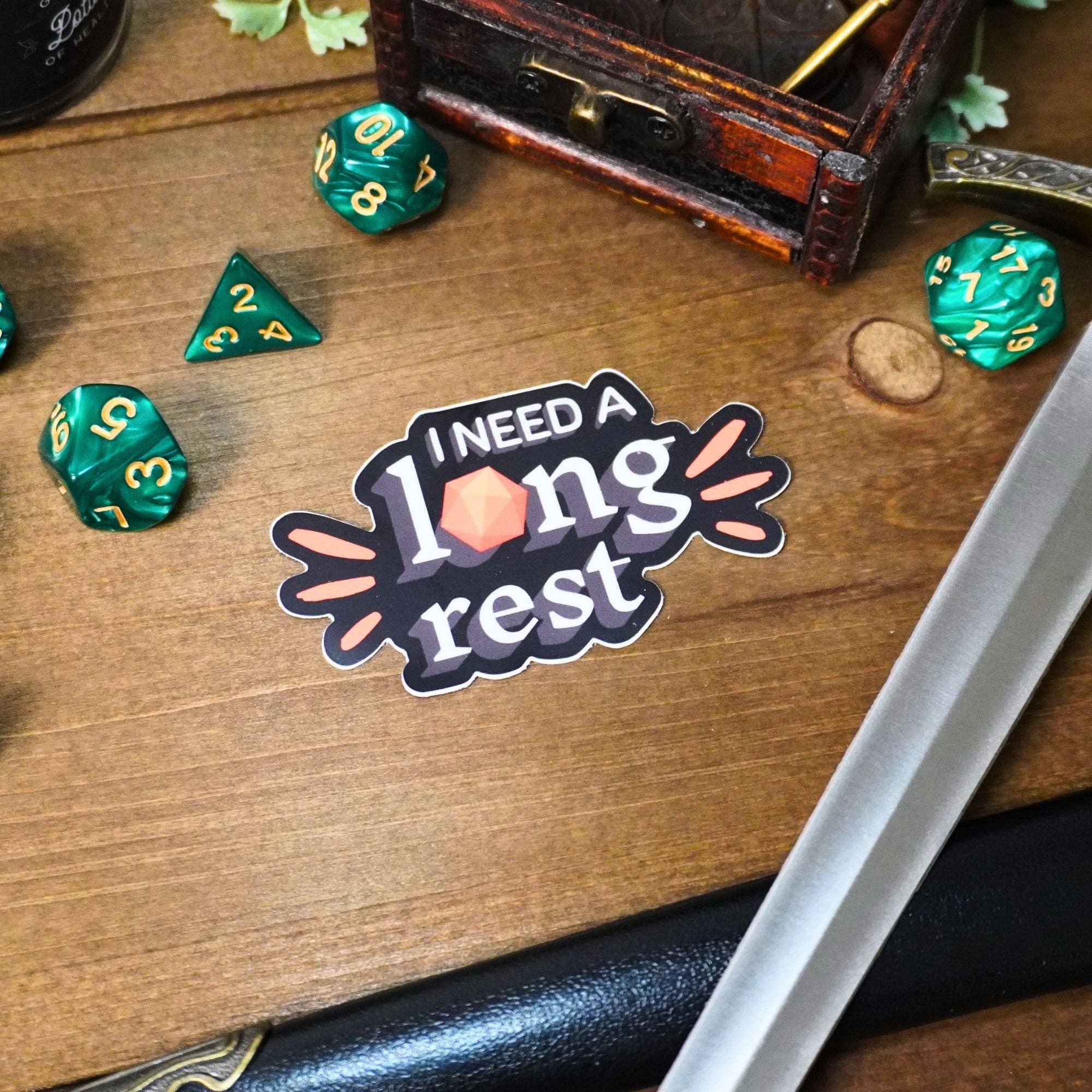 I Need a Long Rest sticker featuring a D20 die, sword, and chest for tabletop RPG enthusiasts.