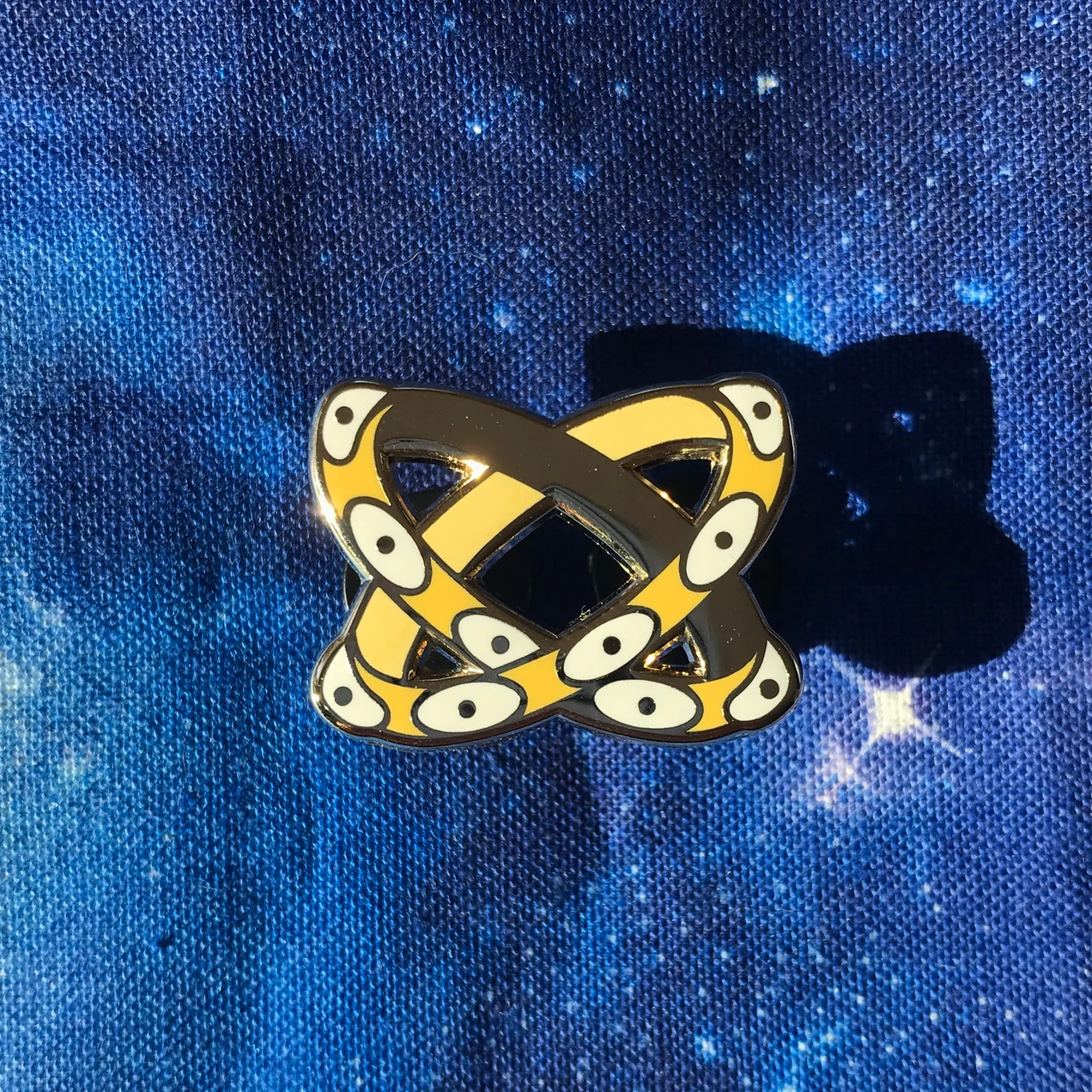 Gold-plated Criss-Crossed Throne Pin with two yellow snakes intertwined on a starry blue background.