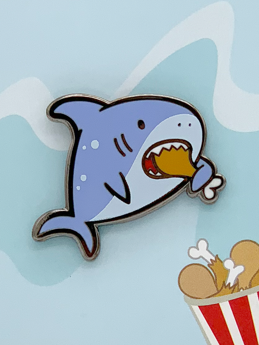 Hungry Shark enamel pin, black nickel plated, shows cartoon shark holding fried chicken and a bucket of chicken legs.
