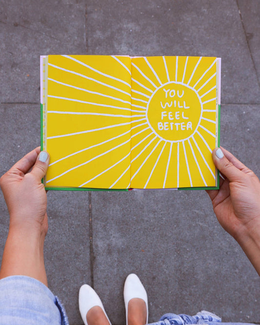 Person holding Its OK to Feel Things Deeply notebook with sun illustration on the cover.