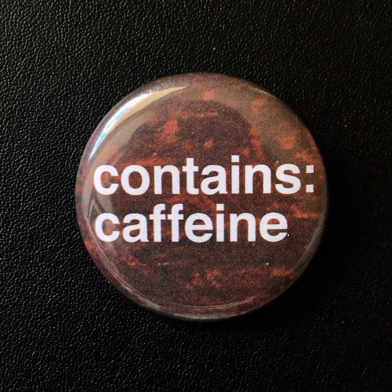 1.25 round pinback button with white text that reads Contains Caffeine on a black background.