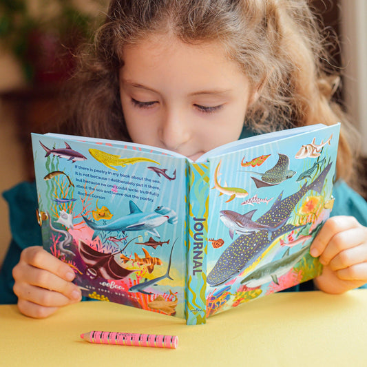 Sharks and Friends Journal on a yellow table with a pink pencil, held by a young girl.