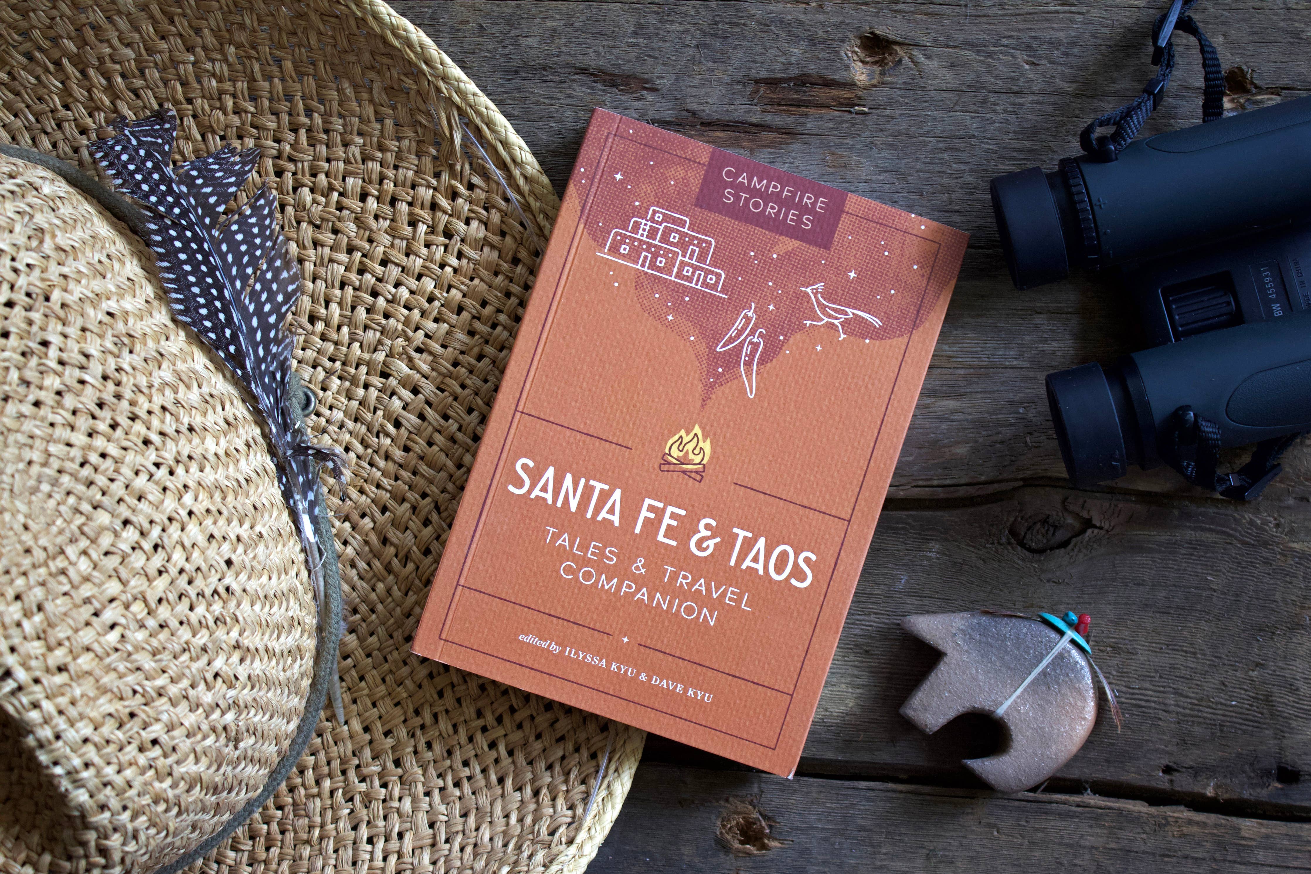 Campfire Stories: Santa Fe & Taos on a table with binoculars, straw hat, and bear totem.
