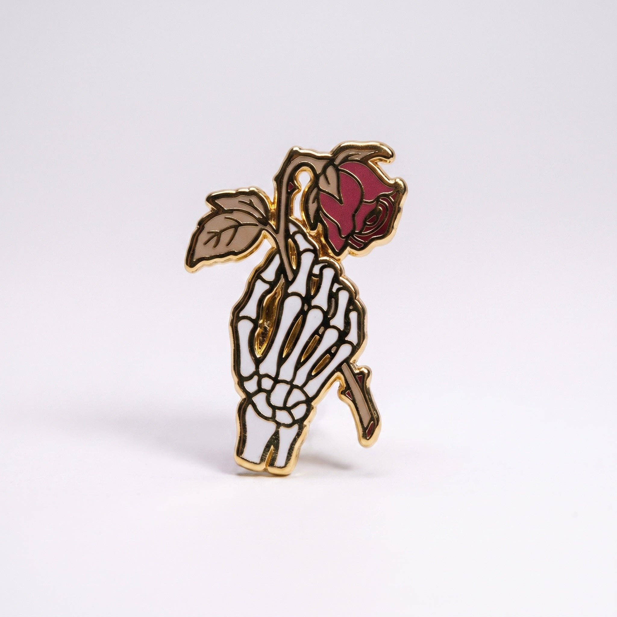 Dead Romantic pin: gold-plated hard enamel pin of a skeletal hand holding a wilted rose.