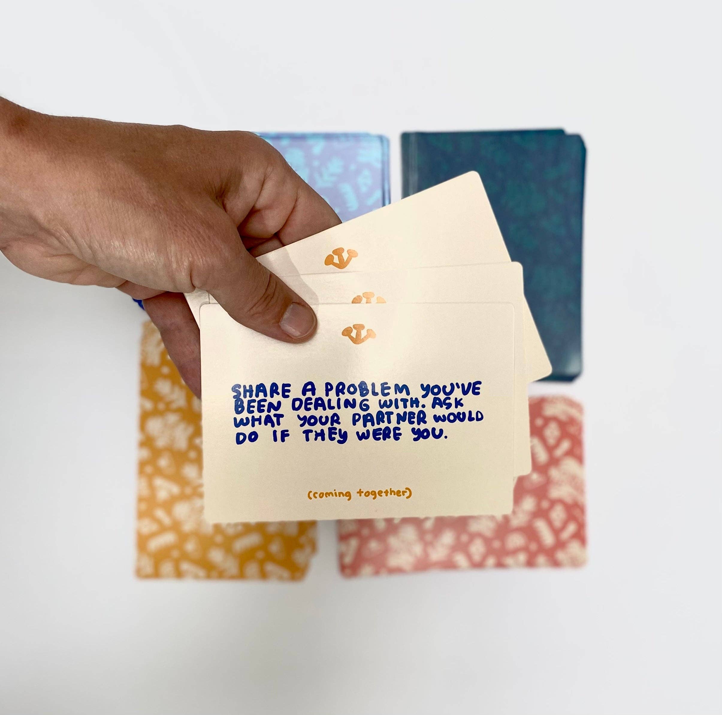 A hand holds A Safe Space For Us Deck cards; the top card features a vulnerability question about sharing a problem.