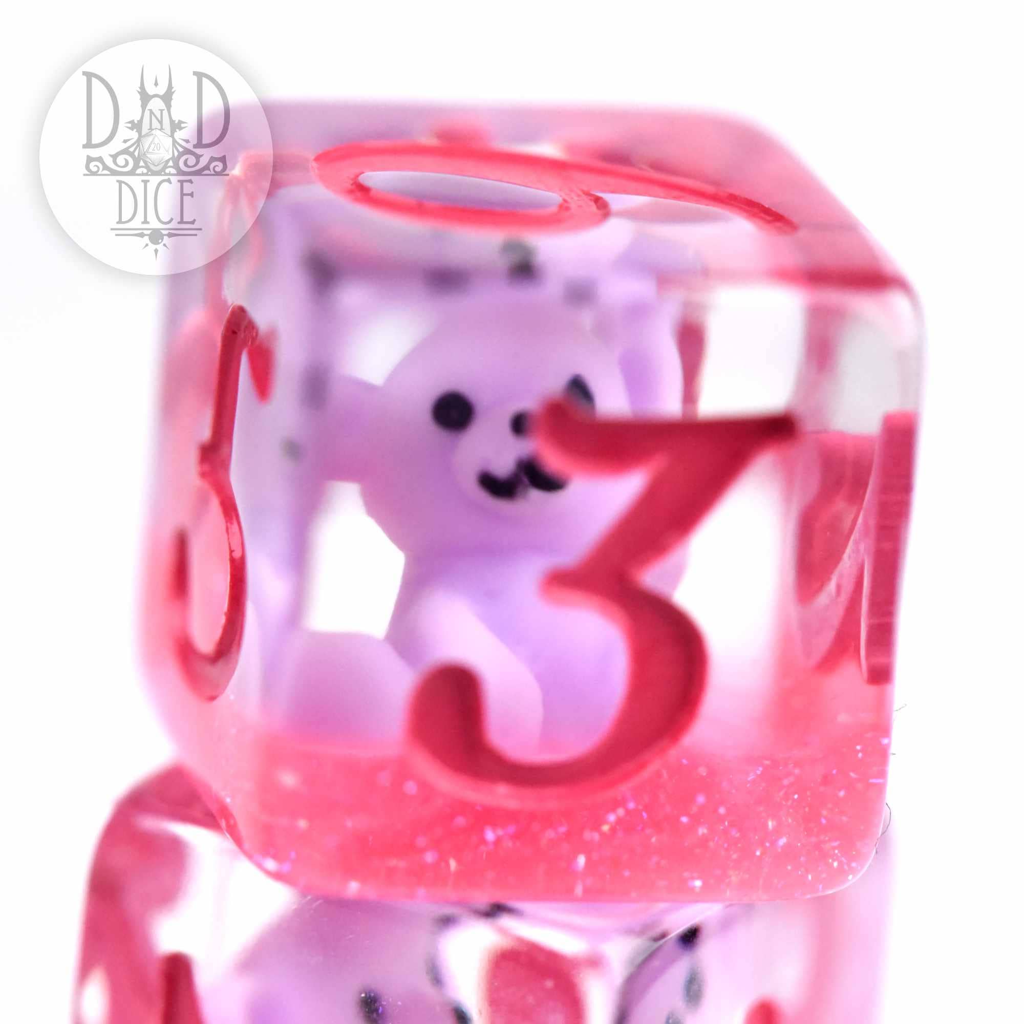 Clear pink resin DND die with red numbers and a small purple bear figurine inside.